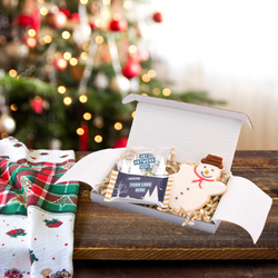 Festive treat box with chocolate coins, a snowman shortbread and chocolate bar with a decorated Christmas tree behind them. 