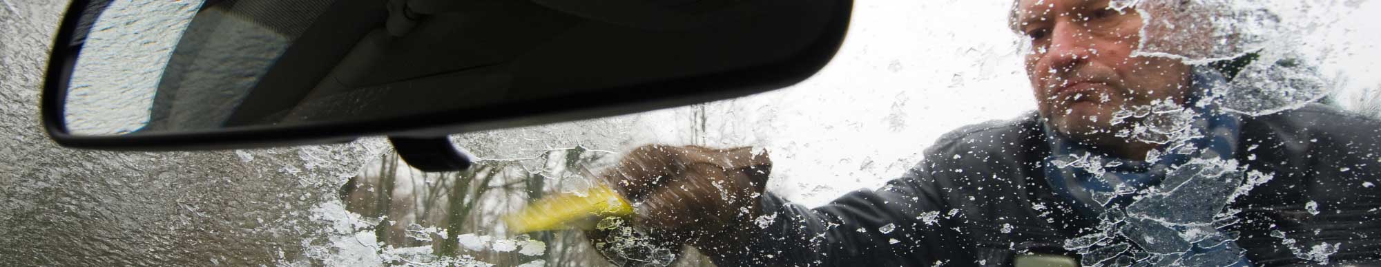 Man using window scraper to scrape snow off of car 