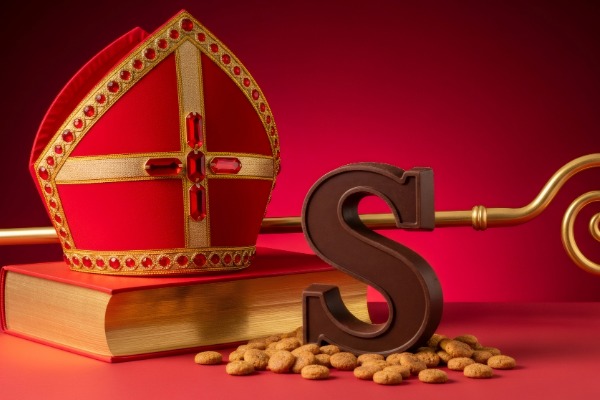 A traditional red Sinterklaas hat with gold trim placed beside chocolate letter S treats.