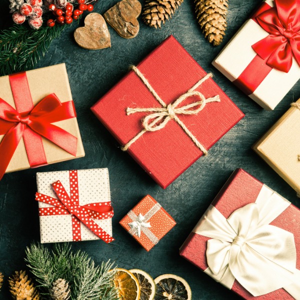 Red Christmas gifts wrapped with ribbon, surrounded by pine cones and red berries on a festive background.